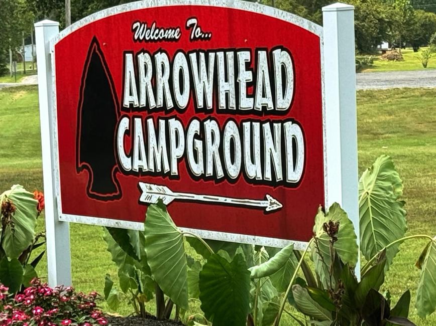 Welcome to Arrowhead Campground sign. Red background with white letters and arrow. Black arrowhead next to the words.
