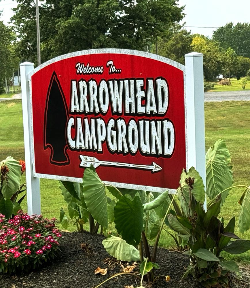 Welcome to Arrowhead Campground sign. Red background with white letters and arrow. Black arrowhead next to the words.