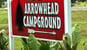 Welcome to Arrowhead Campground sign. Red background with white letters and arrow. Black arrowhead next to the words.